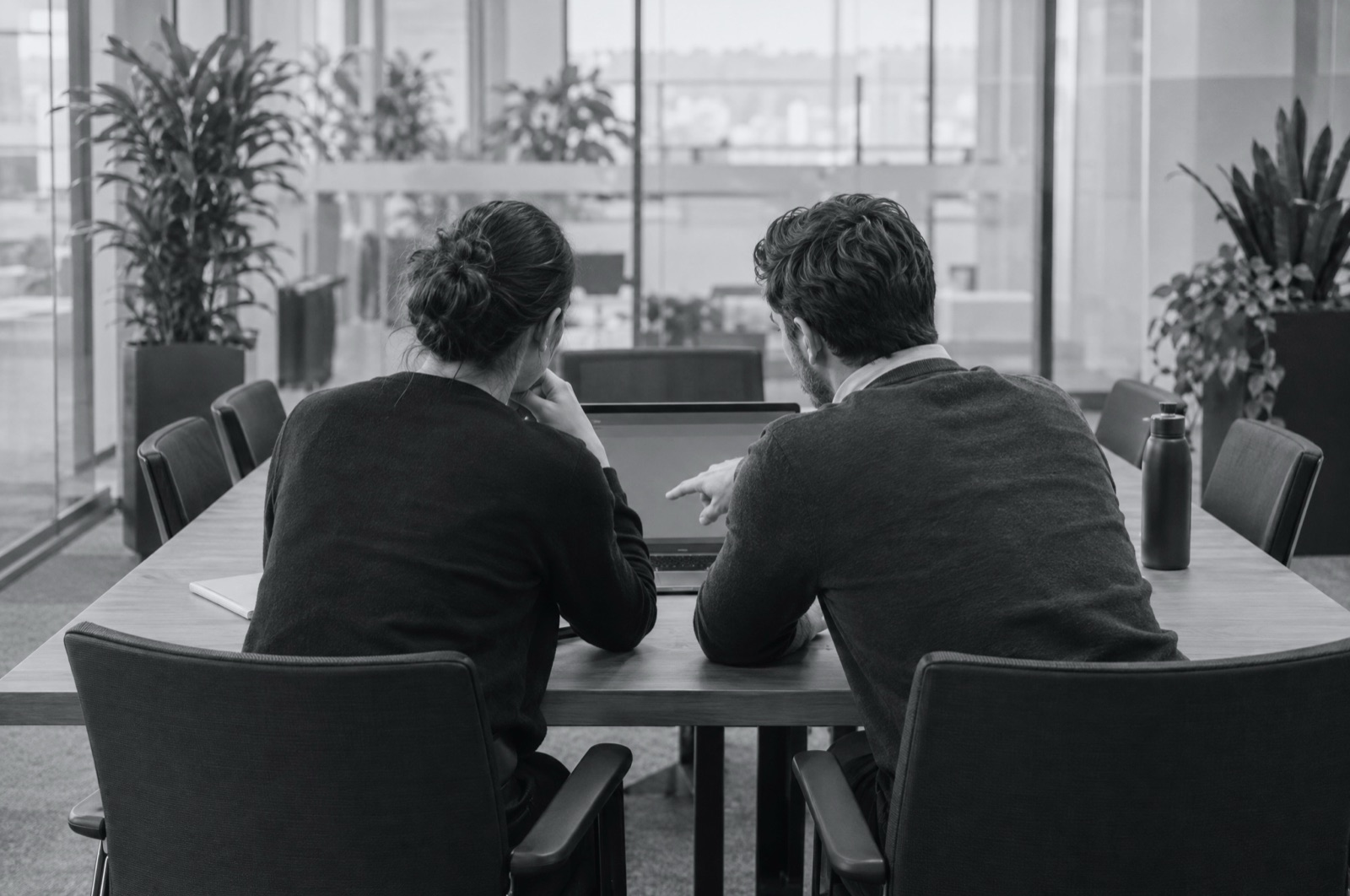 Two operations managers at a head office table reviewing a laptop together