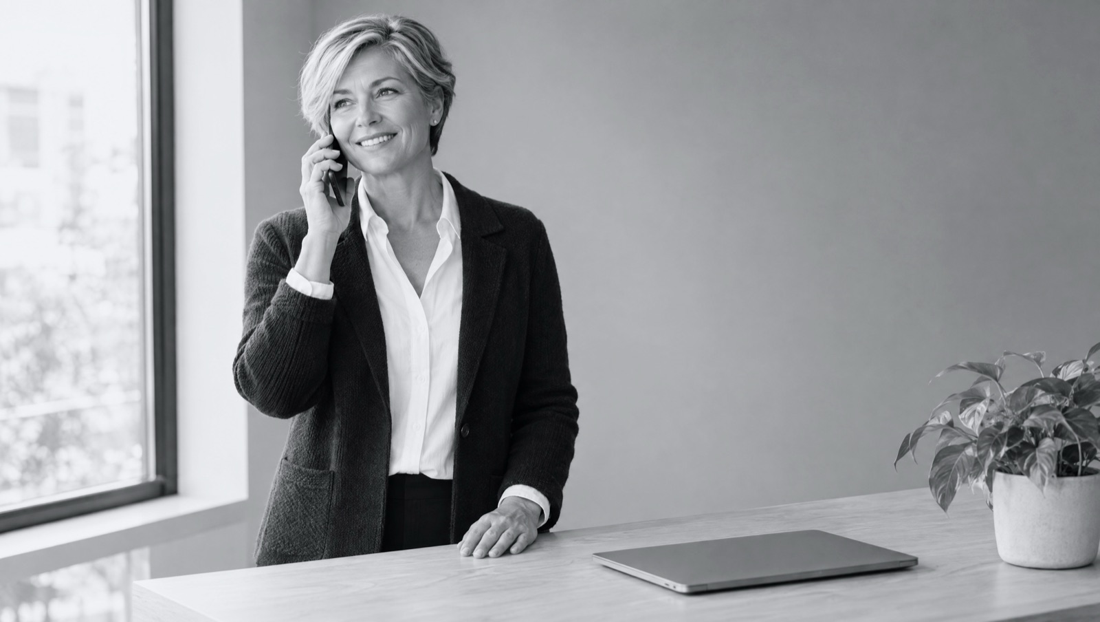 A business owner smiling on a phone call at her desk, a closed laptop in front of her.