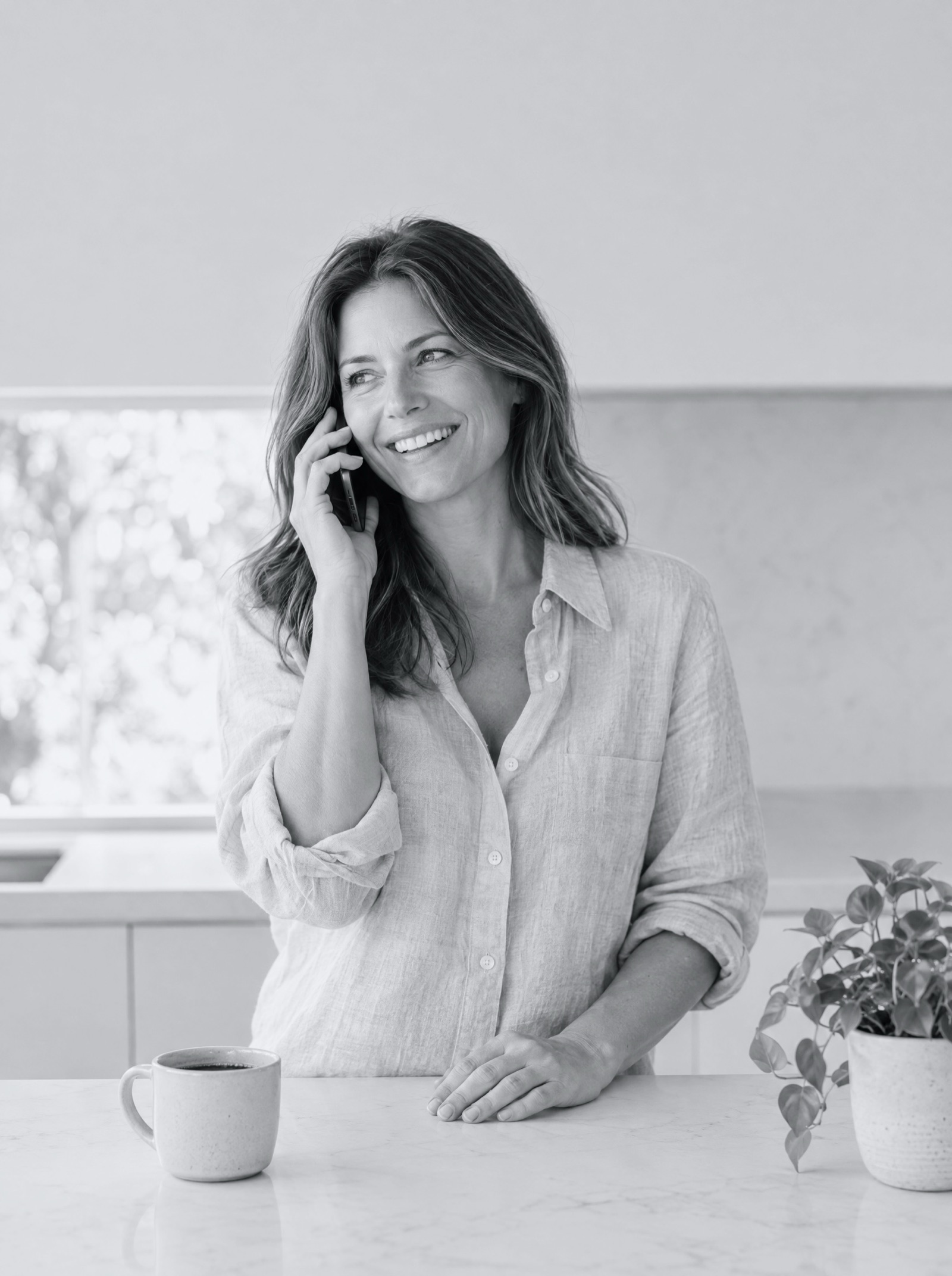 A homeowner smiling on a phone call at a bright kitchen island
